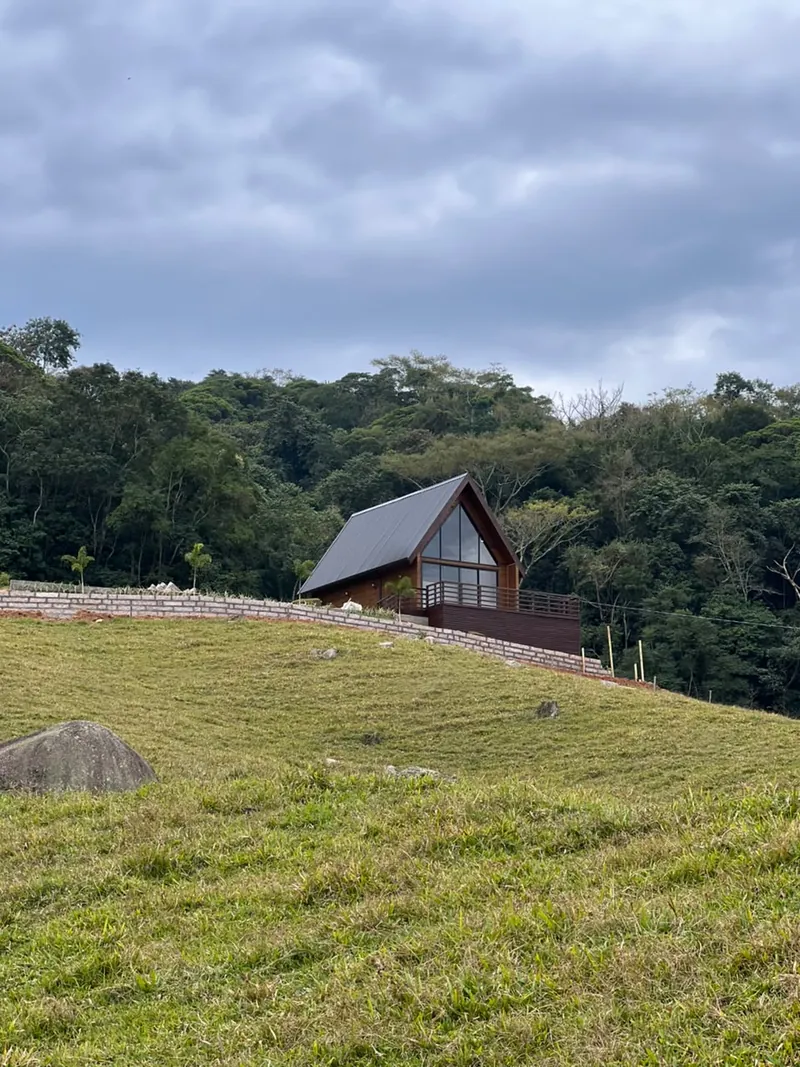 O chalé visto do pasto, com a mata e o céu nublado