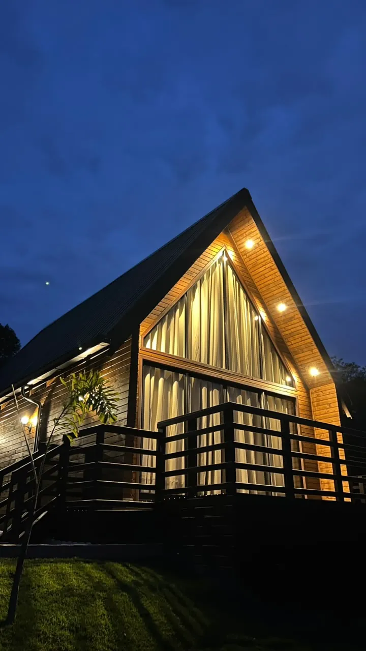O chalé à noite, com o frontão de vidro iluminado e o varal de luzes no beiral
