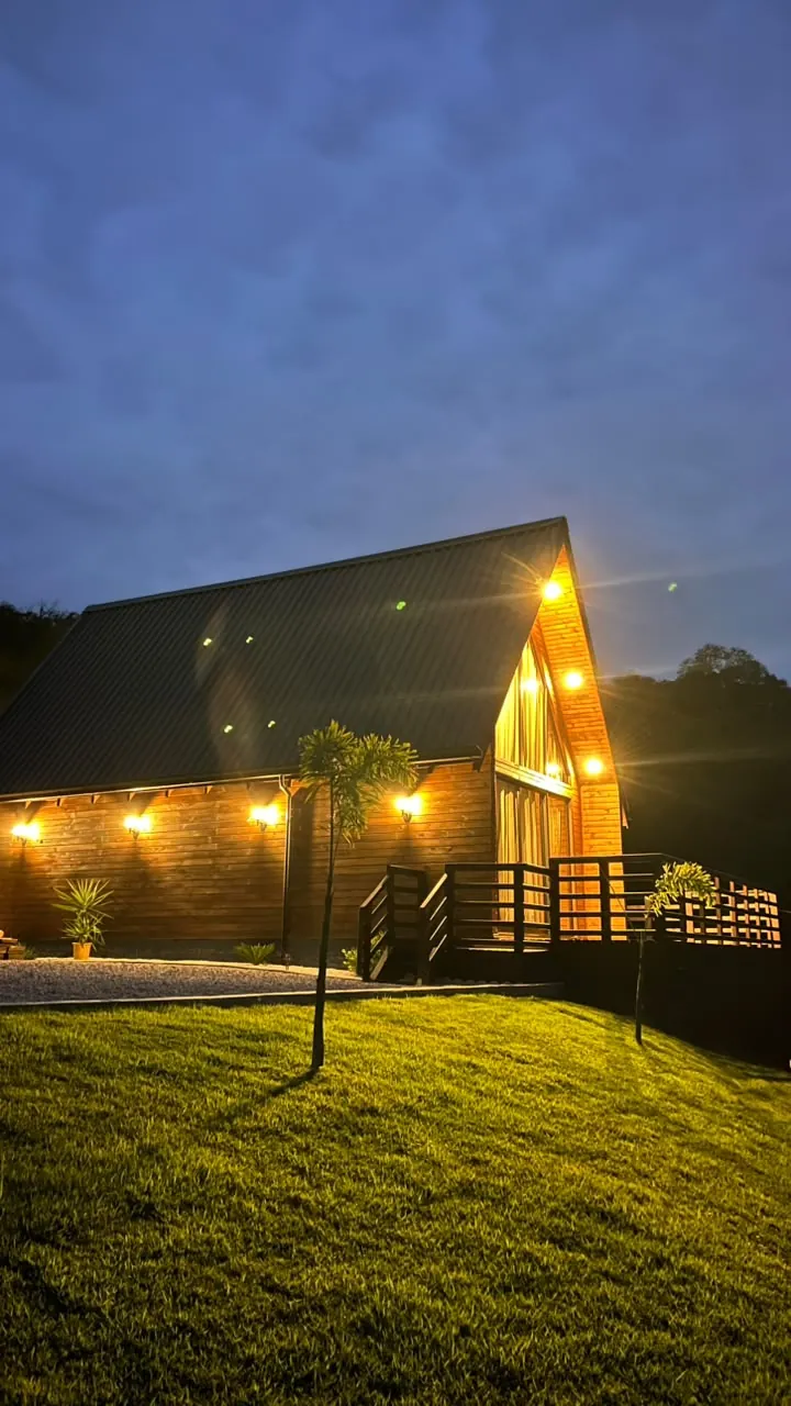 O chalé à noite visto de lado, com o gramado iluminado e o céu escuro